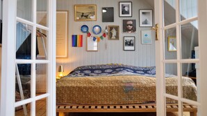 Un dormitorio con una cama, un banco de madera, una pared con cuadros enmarcados y una puerta.