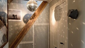 Una escalera con barandilla de madera, una bola de discoteca, una puerta con detalles de piedra y una foto enmarcada en la pared.