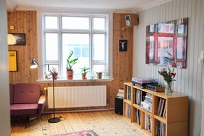 A room with a wooden floor, a window with blinds, a radiator, a bookshelf, a purple chair, and a floor lamp. - Spacious penthouse in the heart of Reykjavik city (Reykjavík)