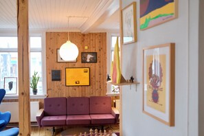 Et værelse med træpaneler, en lilla sofa, en hængende lampe og indrammede kunstværker.