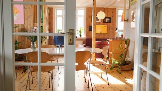 Una habitación con pisos de madera, una mesa de comedor con sillas, un sofá, una lámpara y una planta en maceta.