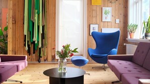 Una habitación con paredes de madera, una silla azul, un sofá morado y una pequeña mesa con un jarrón de flores.