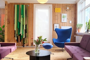 A room with wooden walls, a blue chair, a purple sofa, and a small table with a vase of flowers. - Spacious penthouse in the heart of Reykjavik city (Reykjavík)