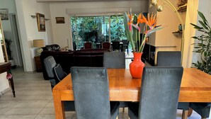 Et spiseområde med et træbord, grå polstrede stole og en klar orange vase med blomster.