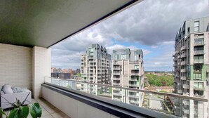 A balcony with a view of modern apartment buildings, a white chair, and a potted plant. - Deluxe Serviced Three Bedroom Apartment (London)