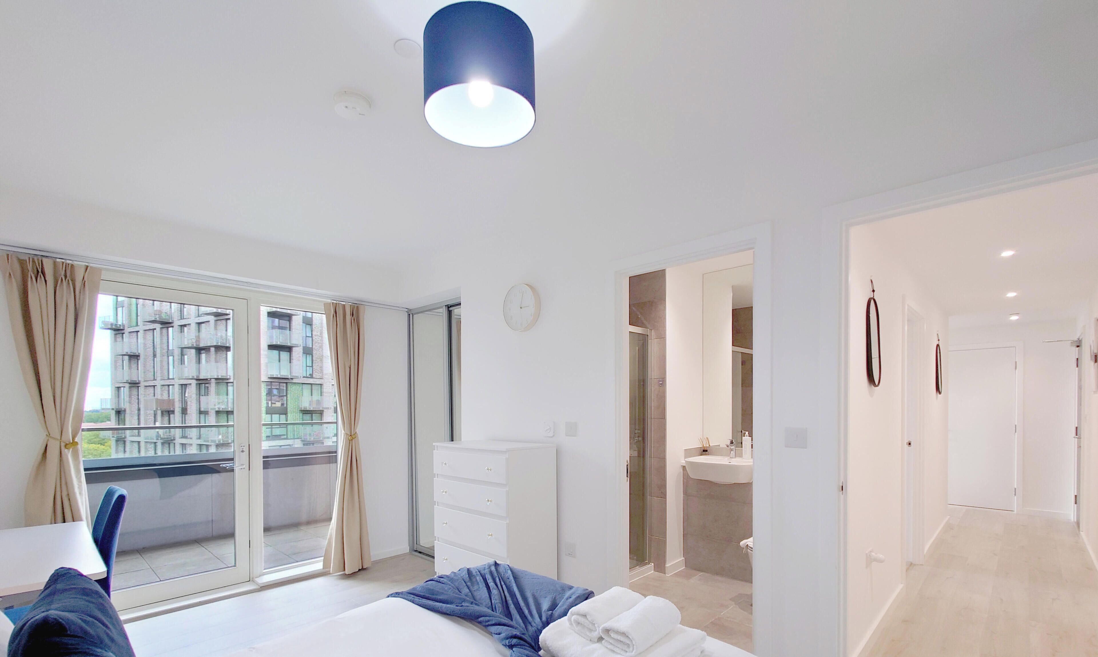 Ett modernt hotellrum med en säng, en byrå, ett badrum med handfat och utsikt över en byggnad genom fönstret.