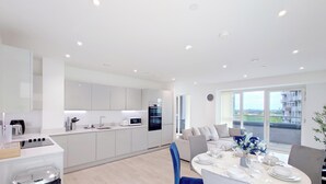 A modern kitchen with white cabinets, a dining area with a table set for four, and a balcony with a view. - Deluxe Serviced Three Bedroom Apartment (London)