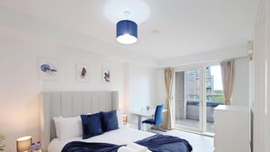 A hotel room with a bed, a desk, a chair, and a balcony with a view. - Deluxe Serviced Three Bedroom Apartment (London)