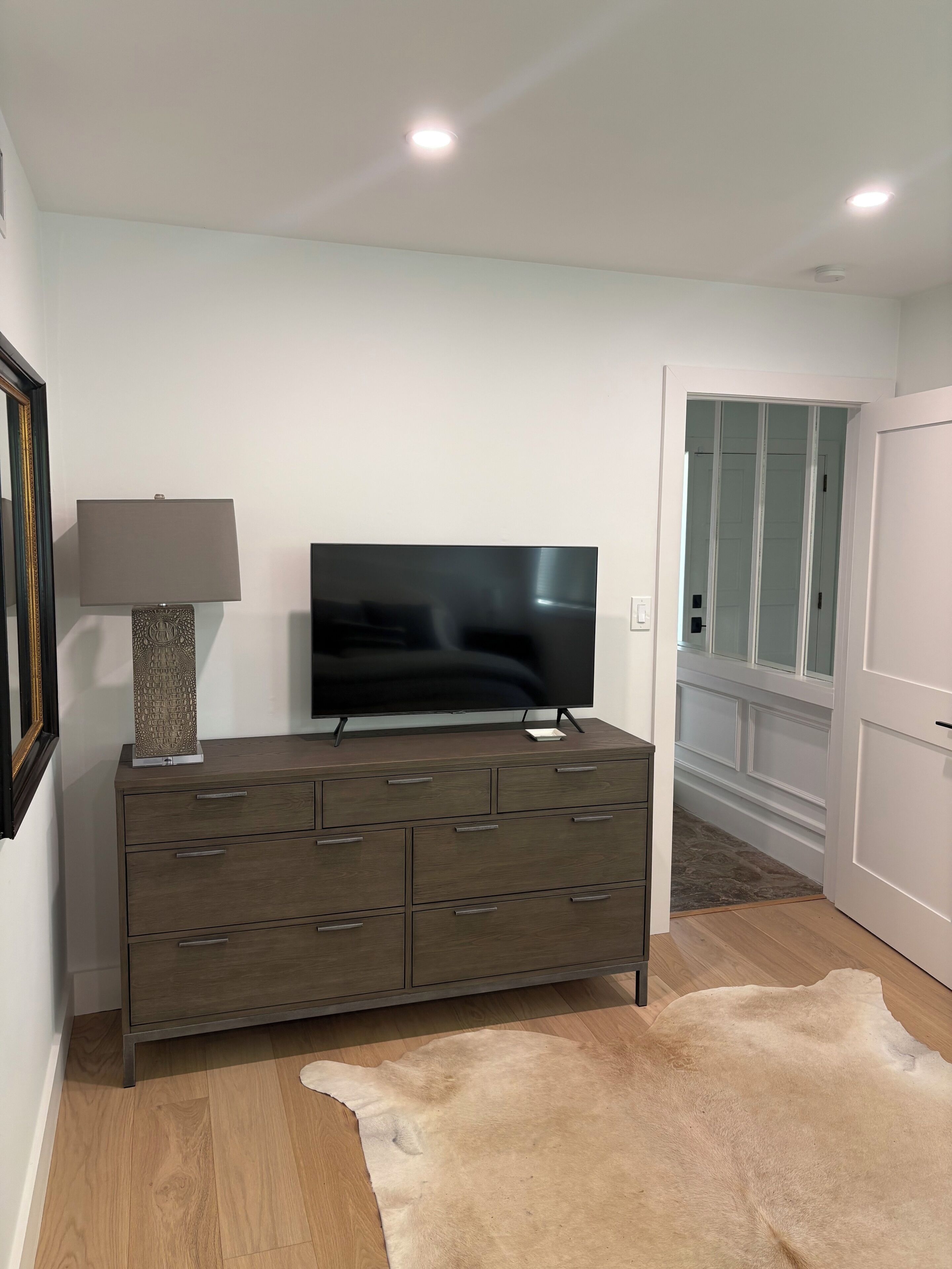 A modern living room with a flat-screen TV on a wooden cabinet, a lamp, and a fur rug.
