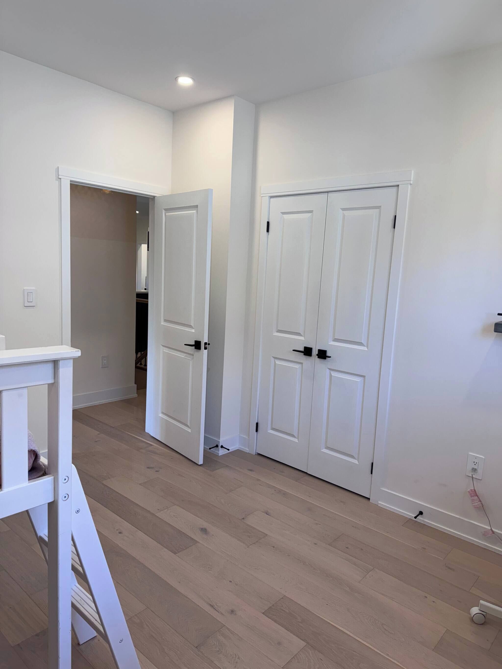 A hallway with two white doors, a white bench, and a light switch on the wall.