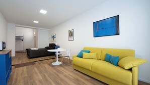 Una sala de estar moderna con un sofá amarillo, una mesa blanca y una obra de arte azul en la pared.