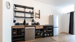 Cocina compacta con lavavajillas, horno y refrigerador, armarios de madera y un reloj en la pared.