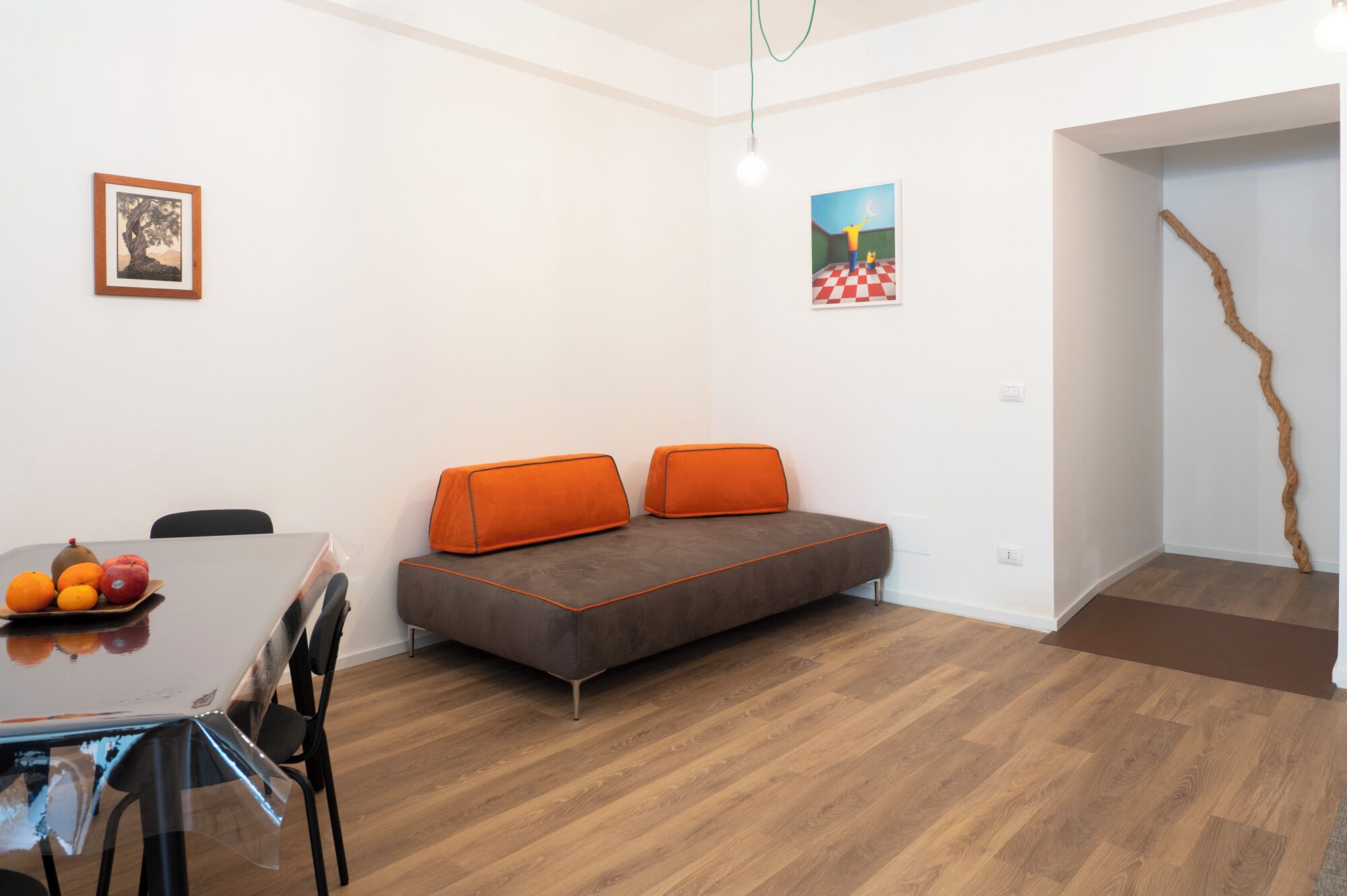 Una habitación moderna con sofá, una mesa de comedor con fruta y obras de arte en las paredes.