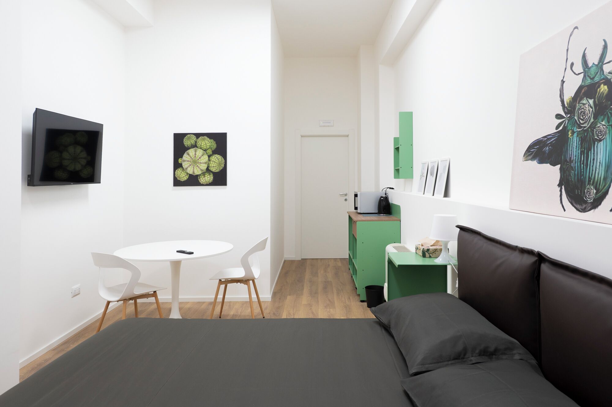 A modern room with a bed, a small round table with chairs, a desk with a lamp, and artwork on the walls.