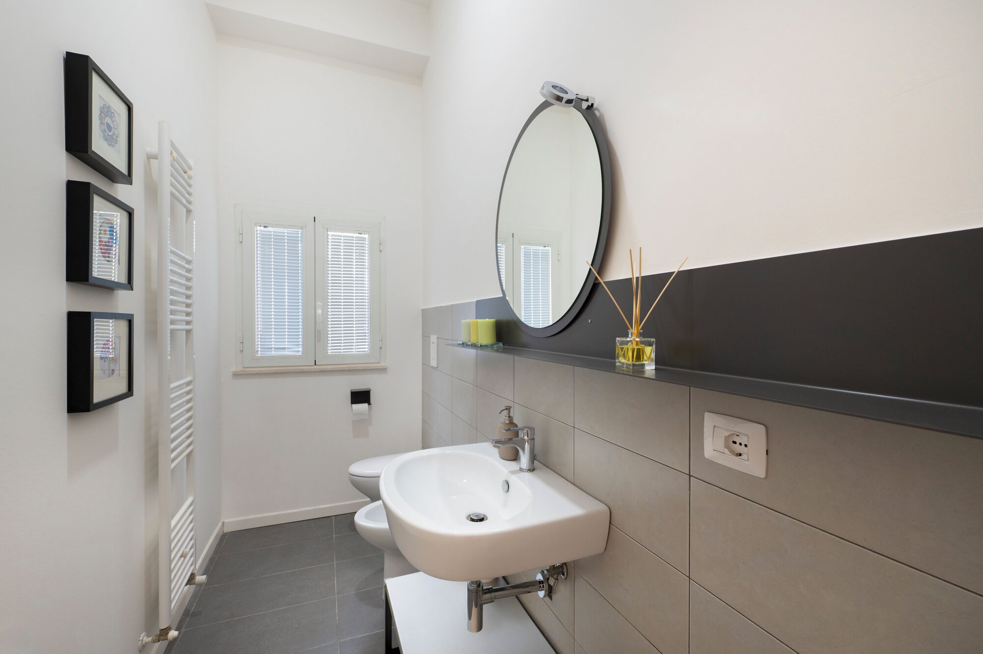 Een moderne badkamer met een witte wastafel, een spiegel en een raam met zonwering.