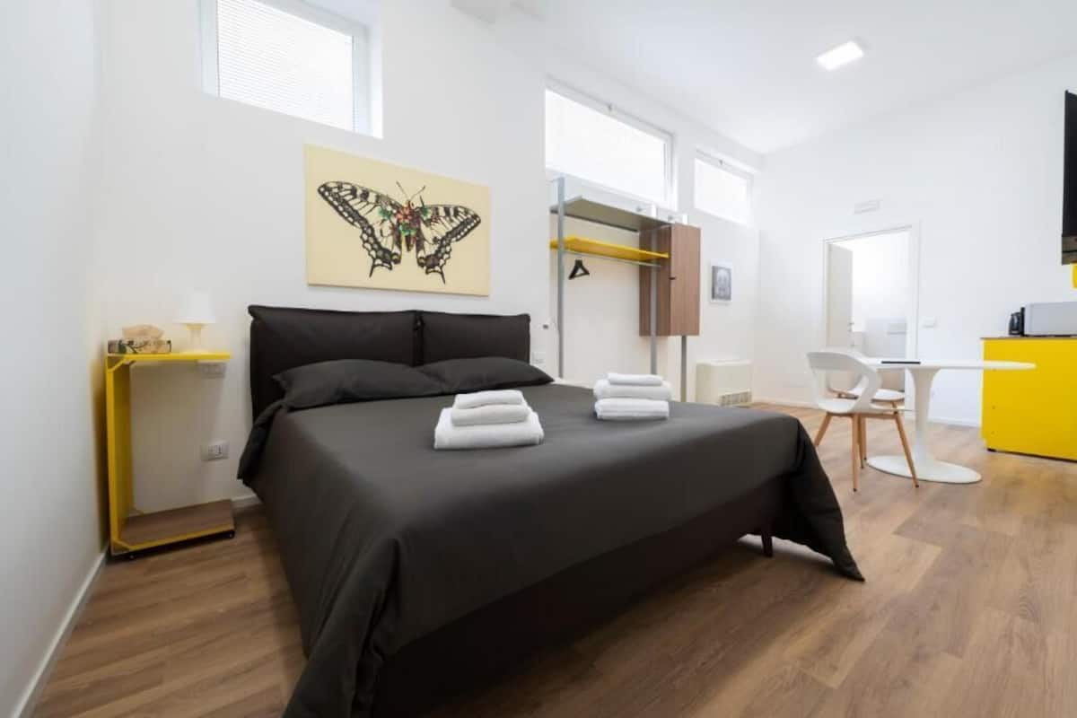 A bedroom with a bed, a desk, a chair, a shelf, and a butterfly artwork on the wall.