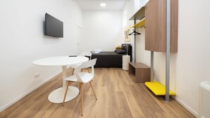Una habitación moderna y funcional con una mesa redonda, dos sillas, una cama, un armario y un televisor de pantalla plana.