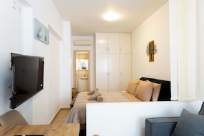 Ein Schlafzimmer mit einem Bett, einem an der Wand montierten Fernseher, einem Kleiderschrank und einem kleinen Tisch.