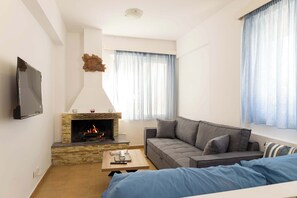A living room with a fireplace, a sofa, a coffee table, and a TV mounted on the wall. - Sinani Beachfront Gems Rhodes - Jacuzzi Apartment (Pefki)