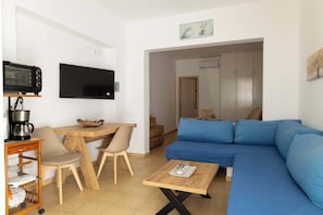 A living room with a blue sofa, a wooden coffee table, a TV, and a kitchenette area.