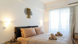 Un lit bien fait, avec une couette et des oreillers de couleur beige, une table de chevet avec une lampe et une œuvre d’art accrochée au mur.