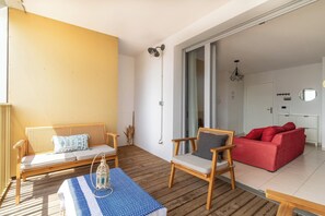 Une pièce avec un plancher en bois, un canapé rouge, une chaise en bois, un banc blanc et une nappe bleue à motifs.