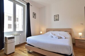 Una habitación de hotel con cama, lámparas de noche, un radiador y una ventana con cortinas.