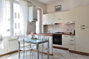 A modern kitchen with a glass dining table, white cabinets, and a view of the street.