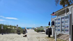 Une propriété située en bord de mer, avec une promenade en bois menant à un bâtiment où sont affichées des annonces de biens immobiliers.