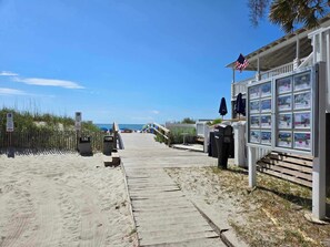 Ein Anwesen am Strand mit einer Holzpromenade, die zu einem Gebäude mit einer Anzeige für Immobilienangebote führt.