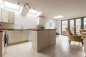 A modern kitchen with a central island, a dining area with floral chairs, and a large sliding glass door leading to an outdoor space.