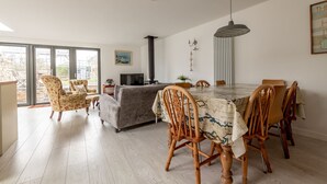 A dining area with a large table, chairs, a sofa, and a TV. - Devon Cottage | Elie (Elie)