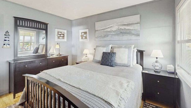 A bedroom with a bed, bedside tables, a dresser, a mirror, and artwork on the walls. - Bodega Bay 2BR ocean-view cottage with hot tub — dog friendly (Bodega Bay)