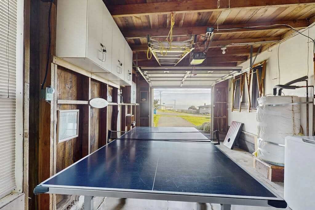 Un pasillo estrecho con una mesa de ping pong, paredes de madera y una puerta de garaje que da a un camino de entrada.
