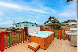 A deck with a hot tub, barbecue grill, and a view of a house.