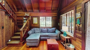 A wooden cabin interior with a sectional sofa, a staircase, and large windows. - Cazadero 1BR A-frame cabin with hot tub for two — dog friendly (Cazadero)