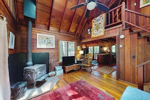 A wooden cabin interior with a wood stove, a television, a rocking chair, and a staircase leading to an upper level. - Cazadero 1BR A-frame cabin with hot tub for two — dog friendly (Cazadero)