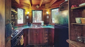 A rustic cabin interior with a wooden ceiling, a central island with a sink, cabinets, and a stove. - Cazadero 1BR A-frame cabin with hot tub for two — dog friendly (Cazadero)