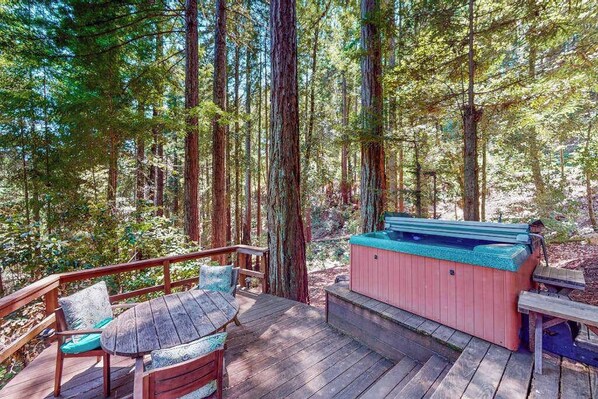 Terraza con jacuzzi, mobiliario de madera y un bosque de fondo.