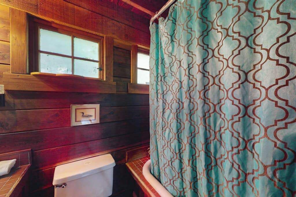 A wooden cabin interior with a toilet, a window, and a patterned curtain.