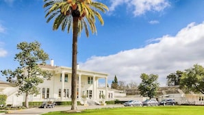 A large white building with a central entrance, surrounded by a well-maintained lawn and parked cars.