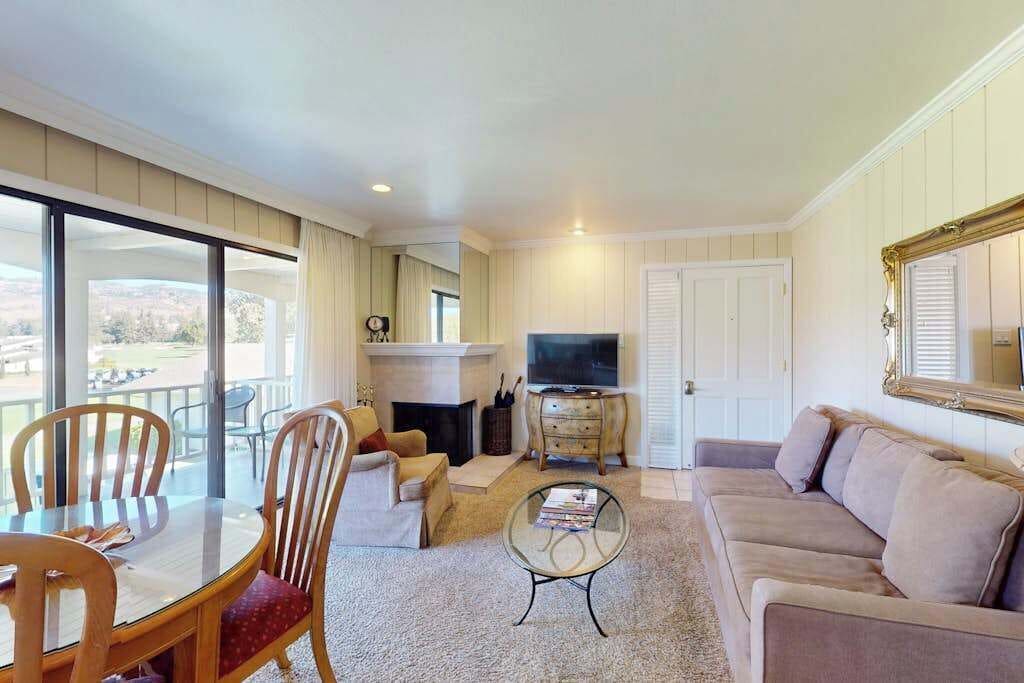 Una sala de estar con sofá, televisión, chimenea, mesa de comedor con sillas y balcón con vistas.