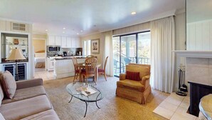 A spacious living room with a sofa, armchair, and coffee table, a kitchen area, and a fireplace.