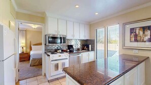 A compact kitchen with white cabinets, a microwave, stove, and a granite countertop.
