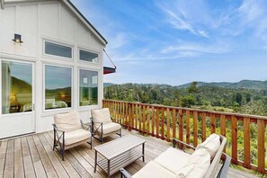 Una terraza con mobiliario exterior, baranda de madera y vistas a un paisaje montañoso.