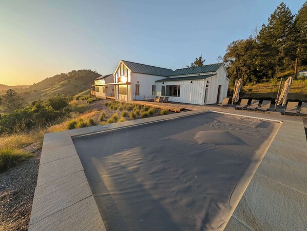 Una casa moderna con una piscina grande, rodeada de un jardín ajardinado con césped y árboles.