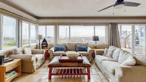A spacious living room with a large window, a ceiling fan, and a view of the outside. - Bodega Bay 3BR ocean-view cottage with hot tub — dogs welcome (Bodega Bay)