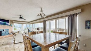 A spacious dining area with a wooden table and chairs, large windows, and a view of the outdoors. - Bodega Bay 3BR ocean-view cottage with hot tub — dogs welcome (Bodega Bay)