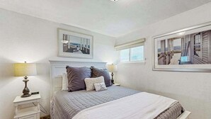 A bedroom with a bed, two bedside tables, a nightstand, a framed picture above the bed, and a window with a view. - Bodega Bay 3BR ocean-view cottage with hot tub — dogs welcome (Bodega Bay)