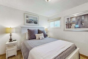 Une chambre à coucher avec un lit, deux tables de chevet, une commode, un tableau encadré au-dessus du lit et une fenêtre donnant sur un beau paysage.